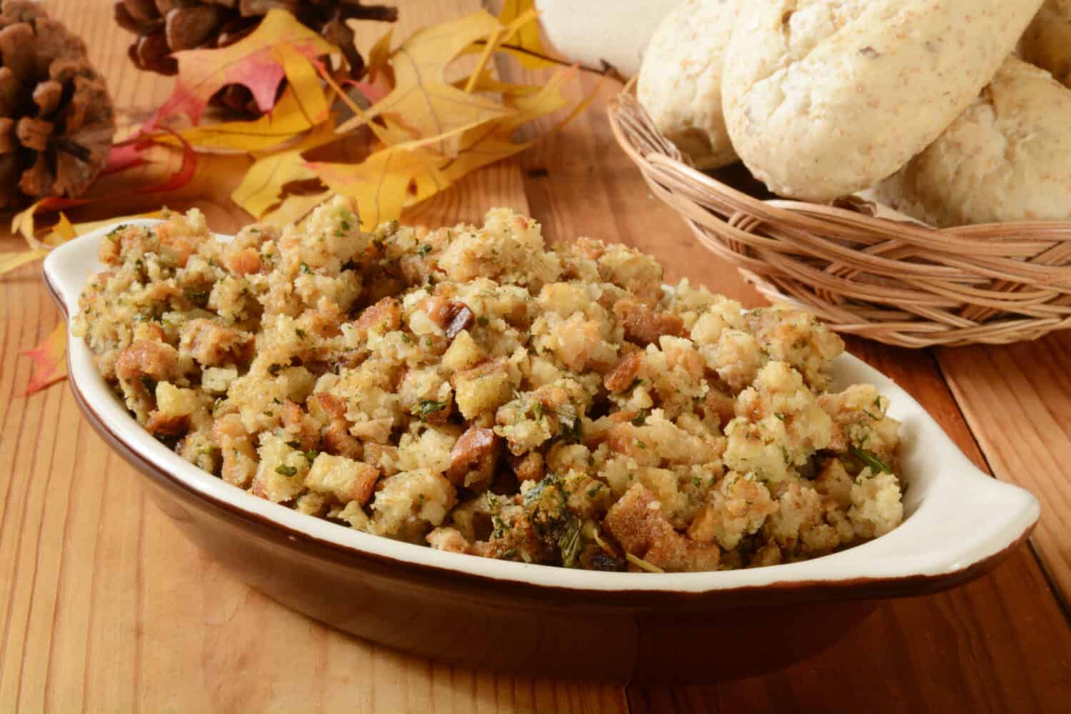 A bowl of turkey stuffing with dinner rolls on a holiday table