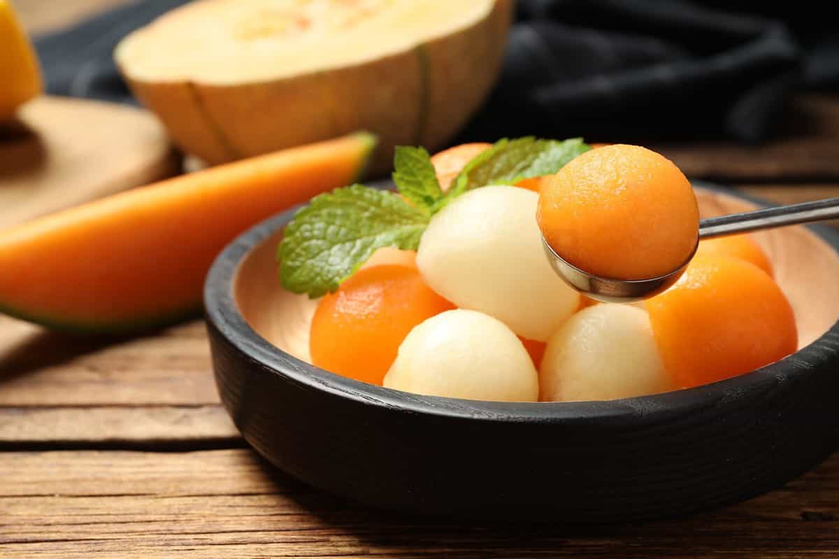 Different melon balls with mint on wooden table, closeup