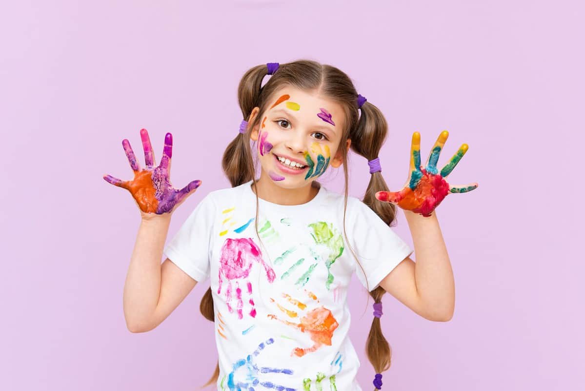 A little girl painted with multicolored paints will playfully have to create on a pink isolated background. Development of children's creativity for schoolchildren.