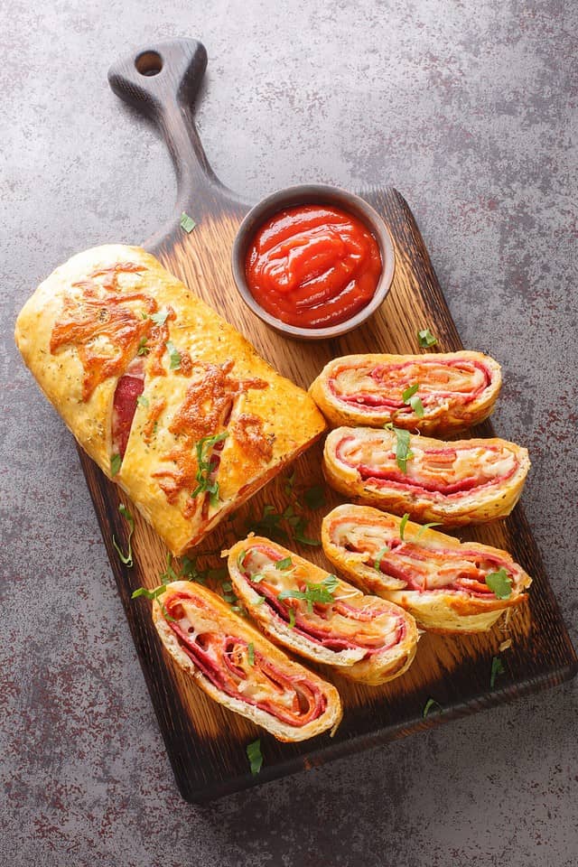 Homemade Stromboli pizza with cheese, pepperoni, salami closeup on the wooden board on the table. Vertical top view from above