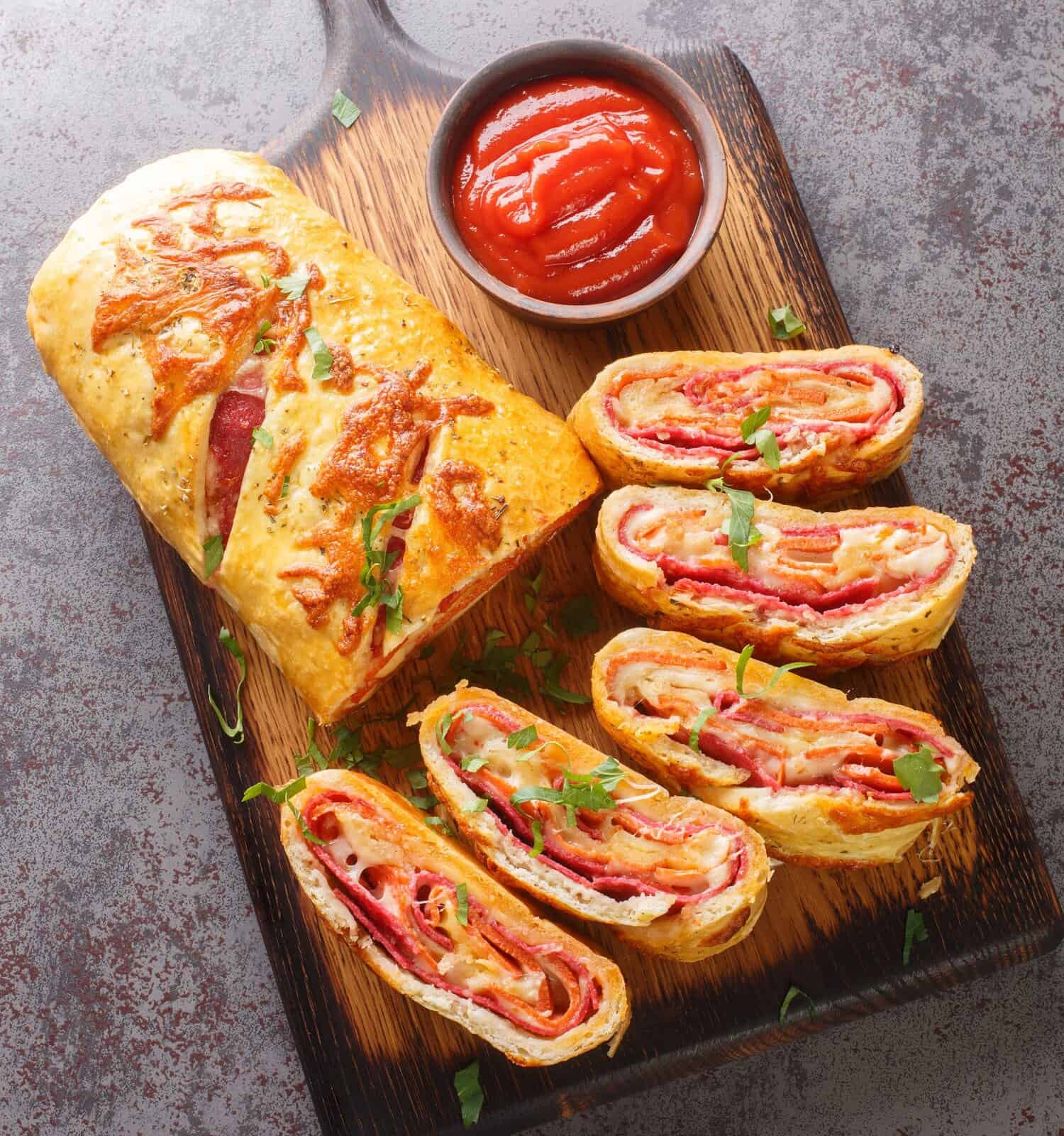 Homemade Stromboli pizza with cheese, pepperoni, salami closeup on the wooden board on the table. Vertical top view from above