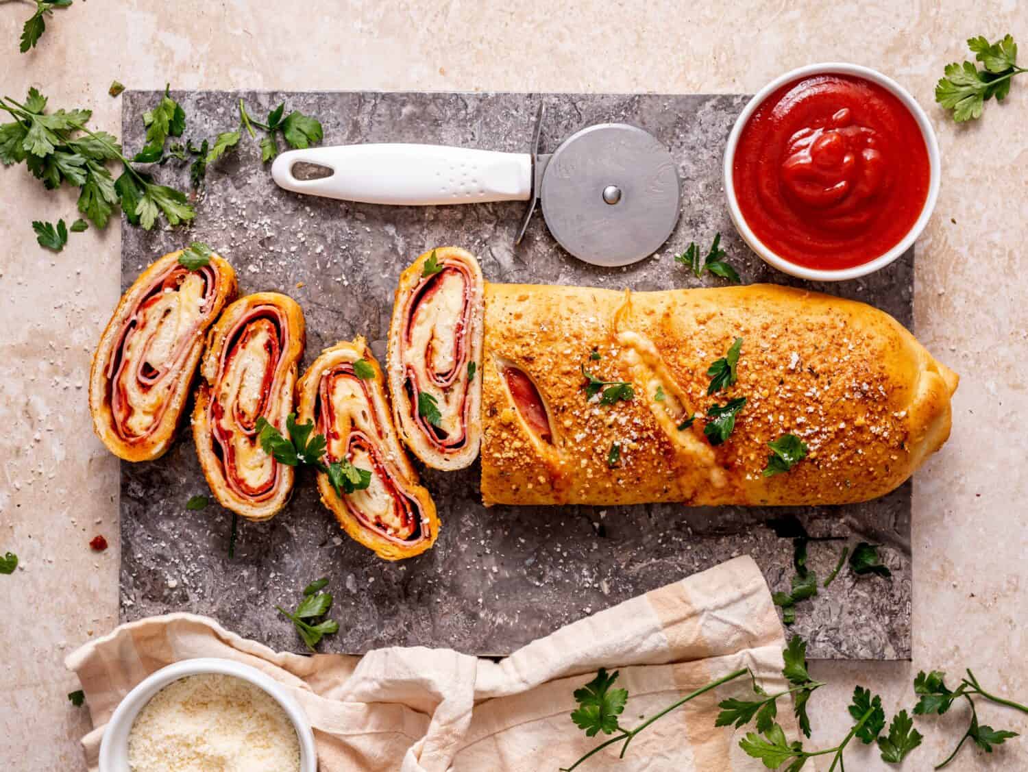 Stromboli pizza sliced on a blue marble served with tomato sauce and parmesan cheese sprinkled with fresh parsley, top view