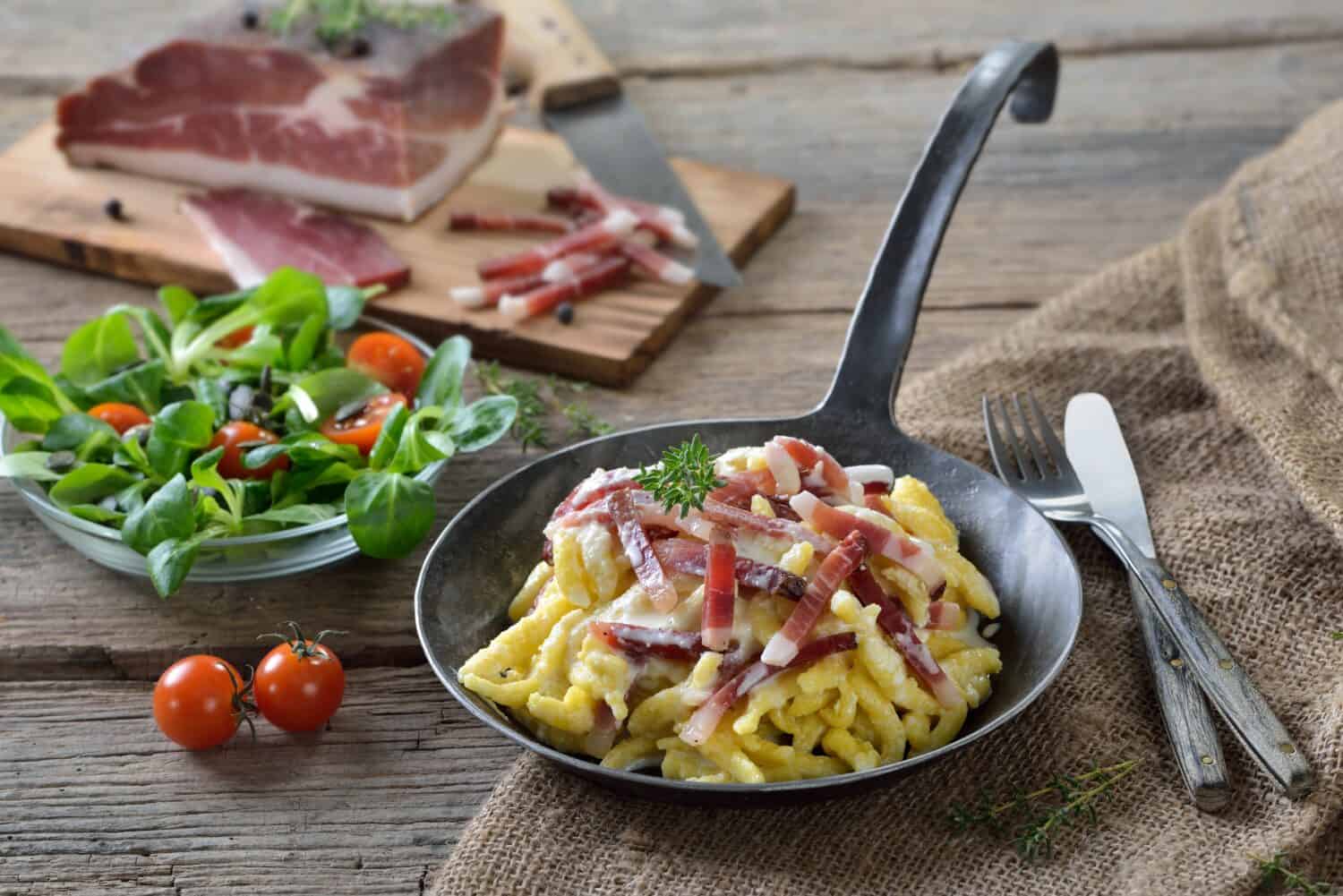 Hearty spaetzle with cheese sauce and South Tyrolean bacon served in an iron frying pan