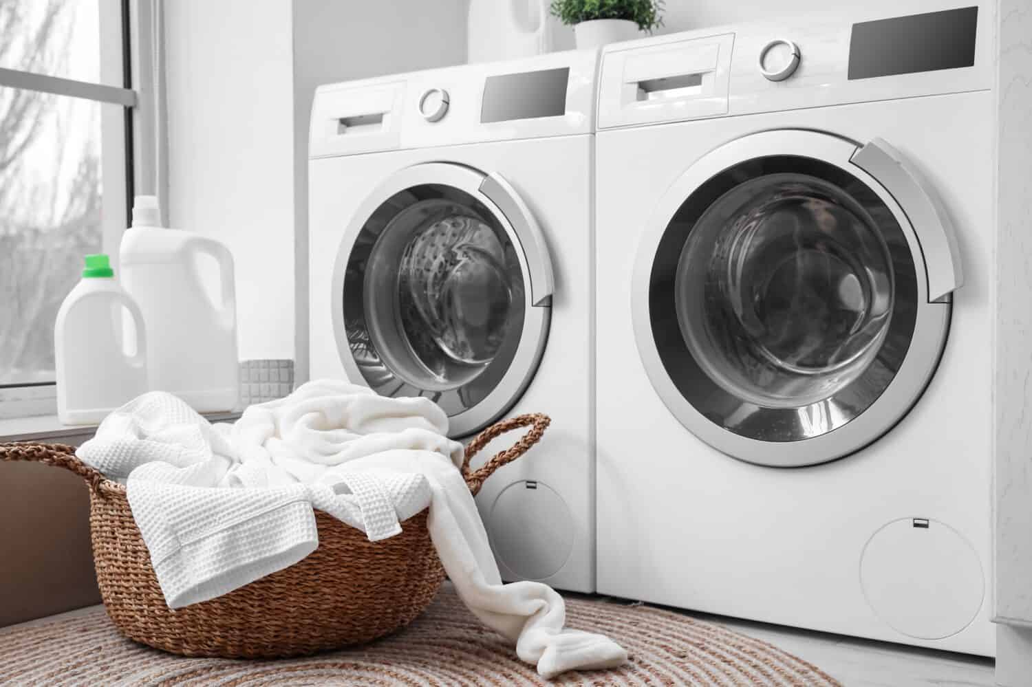 Basket with dirty clothes near washing machines in laundry room