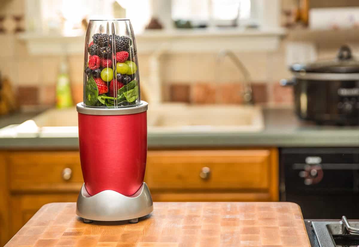 Healthy fruits with small blender on a cutting board getting ready for making a smoothie in a kitchen setting.