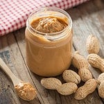 Creamy and smooth peanut butter in jar on wood table. Natural nutrition and organic food. Selective focus.