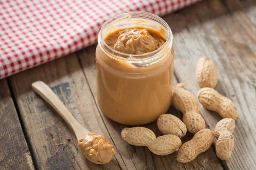 Creamy and smooth peanut butter in jar on wood table. Natural nutrition and organic food. Selective focus.