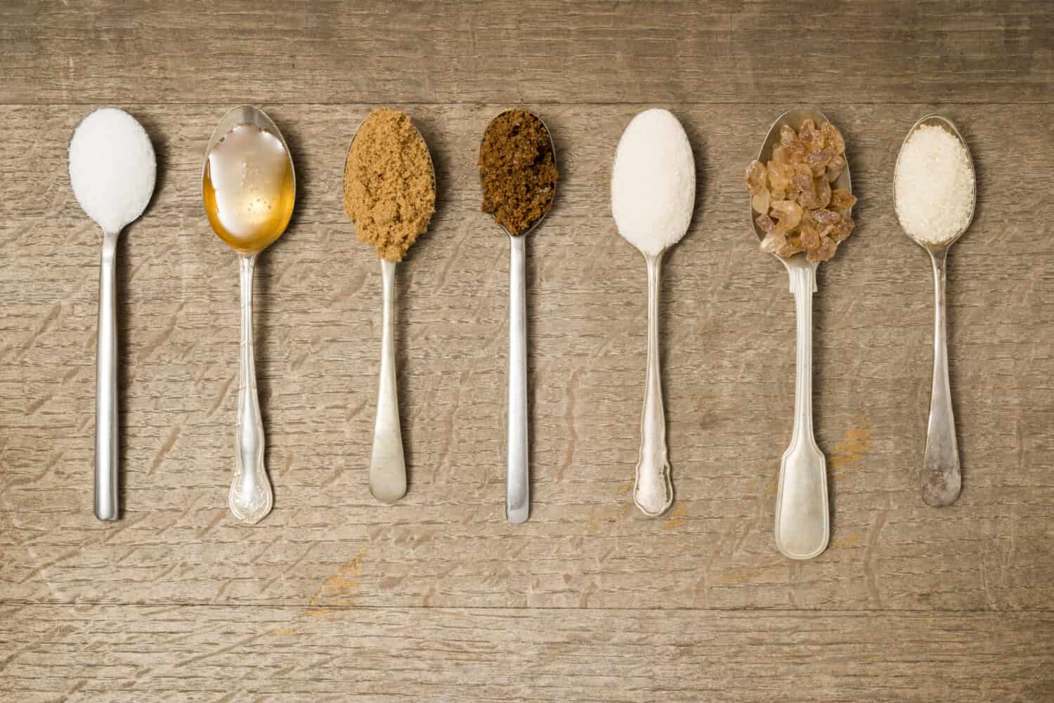 Seven teaspoons in a line with different types of sugar