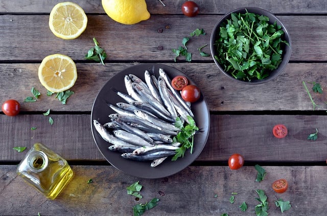 fresh anchovies, placed on a wooden table and accompanied by oil, tomatoes and parsley