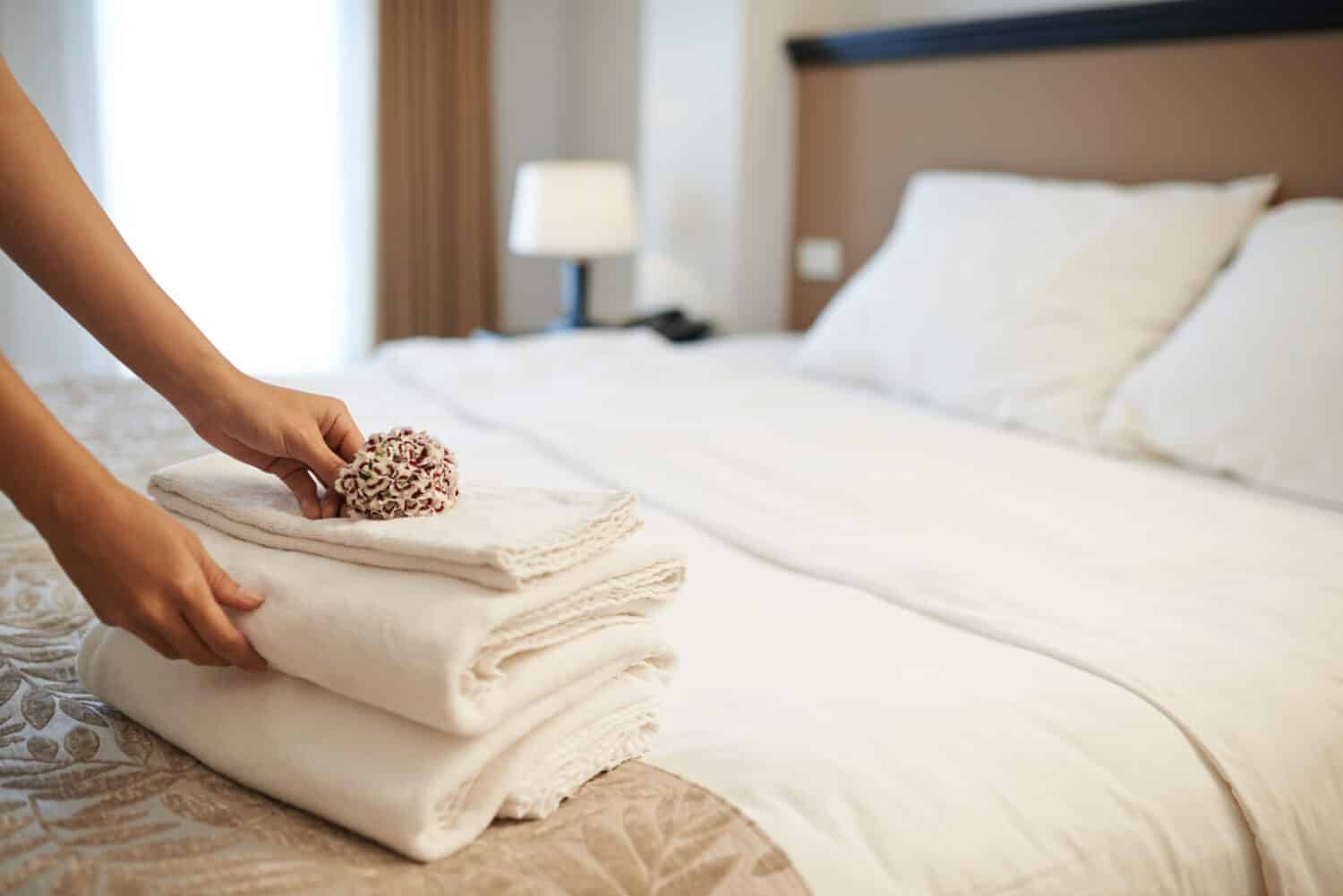 Hands of hotel maid putting flowers on the stack of towels