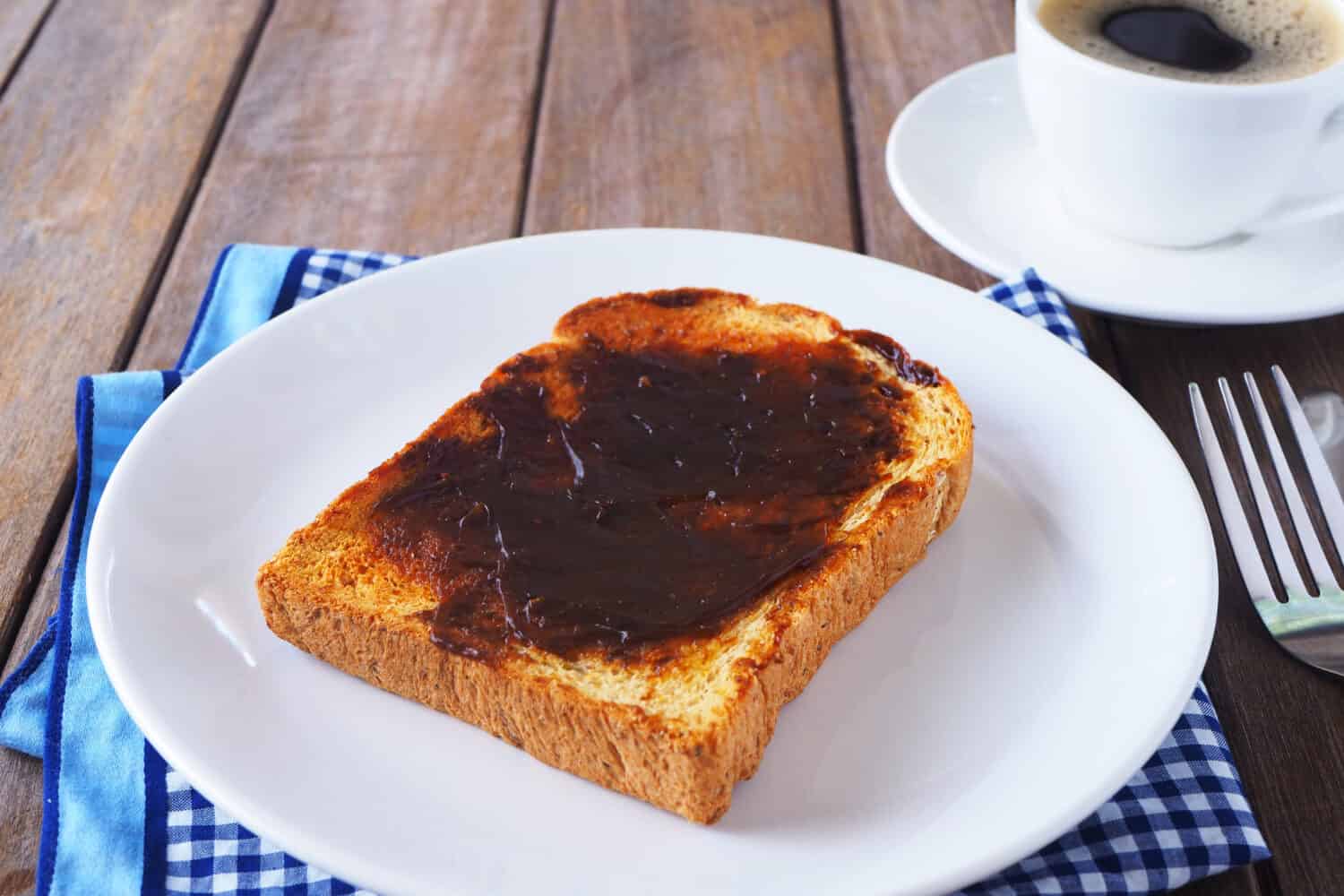 Close up of Australian breakfast with vegemite spread on a sliced wholewheat toast on a wooden table.