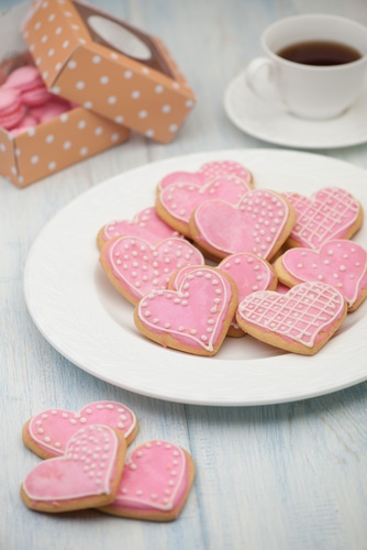 pink cookies in the shape of hearts on a plate and a cup of tea and gift boxes on Valentine's Day