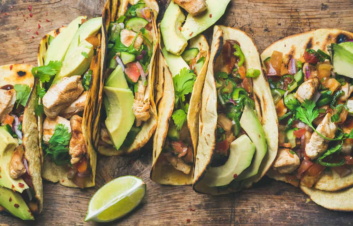 Tacos with grilled chicken, avocado, fresh salsa sauce and limes over rustic wooden background, top view. Healthy low carb and low fat lunch or food for company. Dieting and weight loss concept