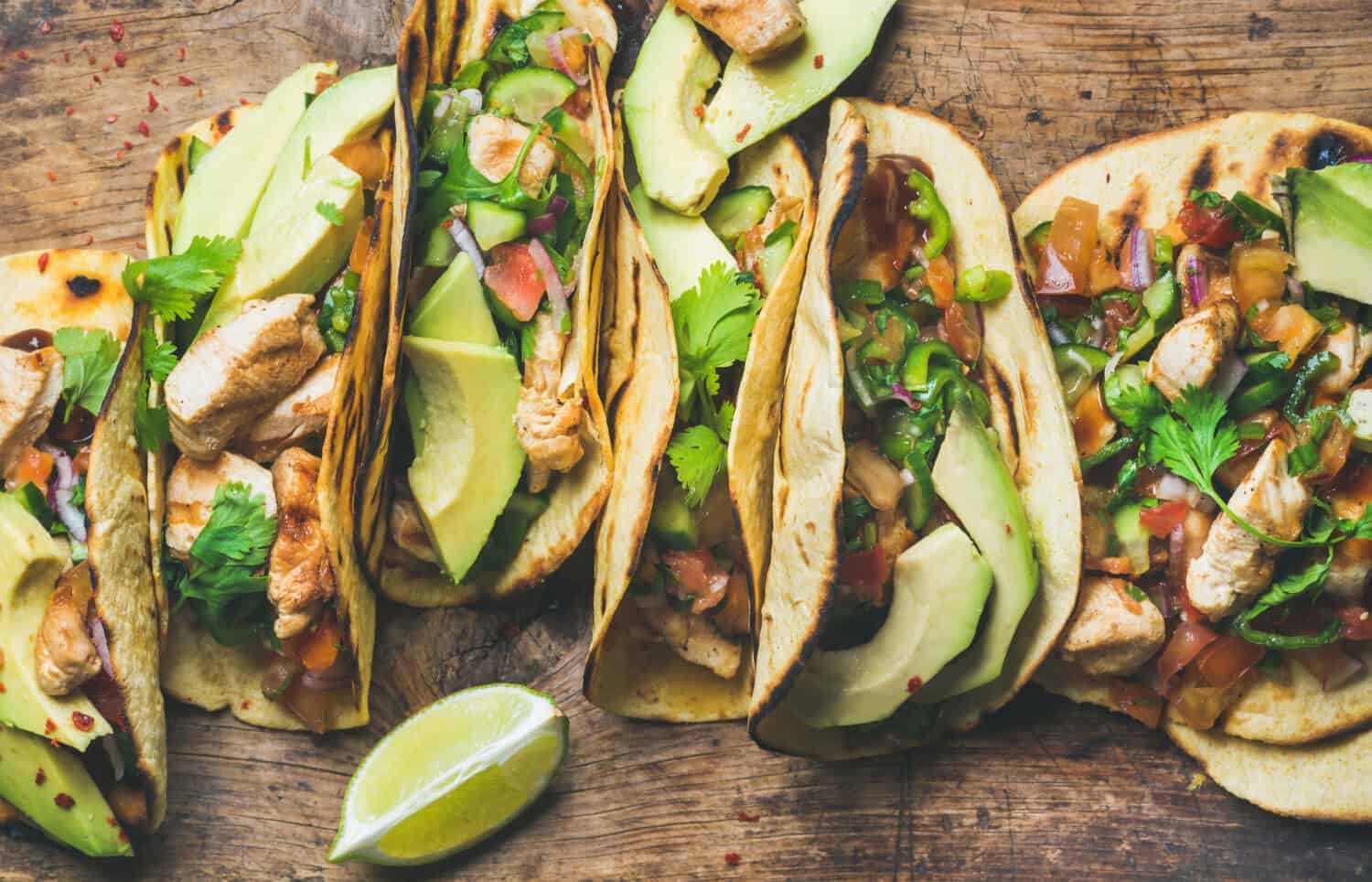 Tacos with grilled chicken, avocado, fresh salsa sauce and limes over rustic wooden background, top view. Healthy low carb and low fat lunch or food for company. Dieting and weight loss concept