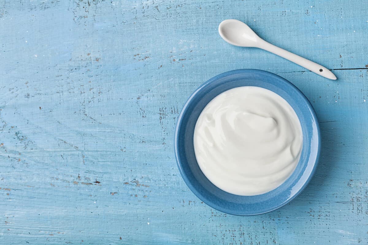 Greek yogurt in blue bowl on rustic wooden table top view.