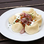 Plate of pierogi or varenyky stuffed filled dumplings with sour cream, bacon and onion, traditional East Europe cuisine meal popular in Poland, Ukraine, Slovakia, Russia, close up, high angle view