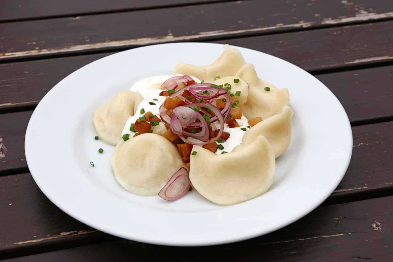 Plate of pierogi or varenyky stuffed filled dumplings with sour cream, bacon and onion, traditional East Europe cuisine meal popular in Poland, Ukraine, Slovakia, Russia, close up, high angle view