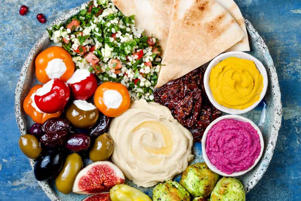 Middle Eastern meze platter with green falafel, pita, sun dried tomatoes, pumpkin and beet hummus.Mediterranean appetizer party idea