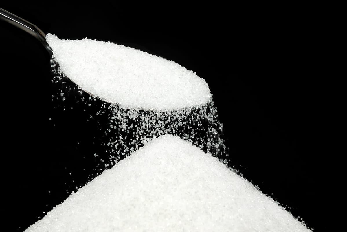 Pouring sugar with a spoon, Selective focus. A pile of ingredient is on Black background, Copy space for your text message or promotional content.