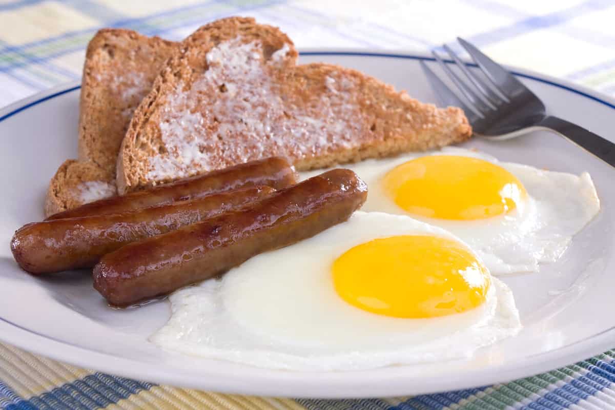 Fried sunny side up eggs with sausage links and buttered wheat toast.