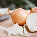 Onion and slices on wooden cutting board.