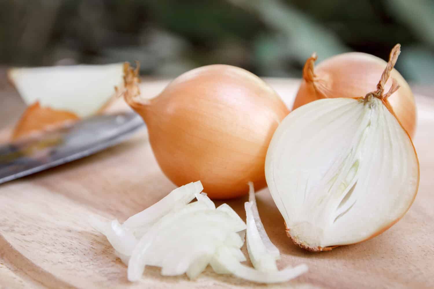 Onion and slices on wooden cutting board.