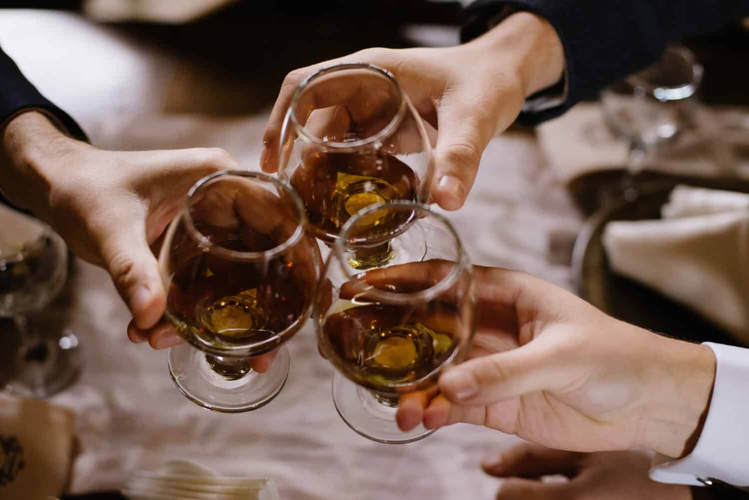 Hands holding the glasses of brandy. Close-up of glasses with cognac in people's hands. Toasting for holiday