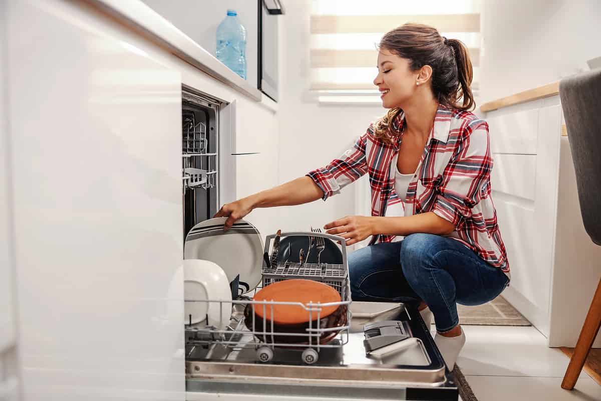 Diligent housewife putting dishes into dishwasher.