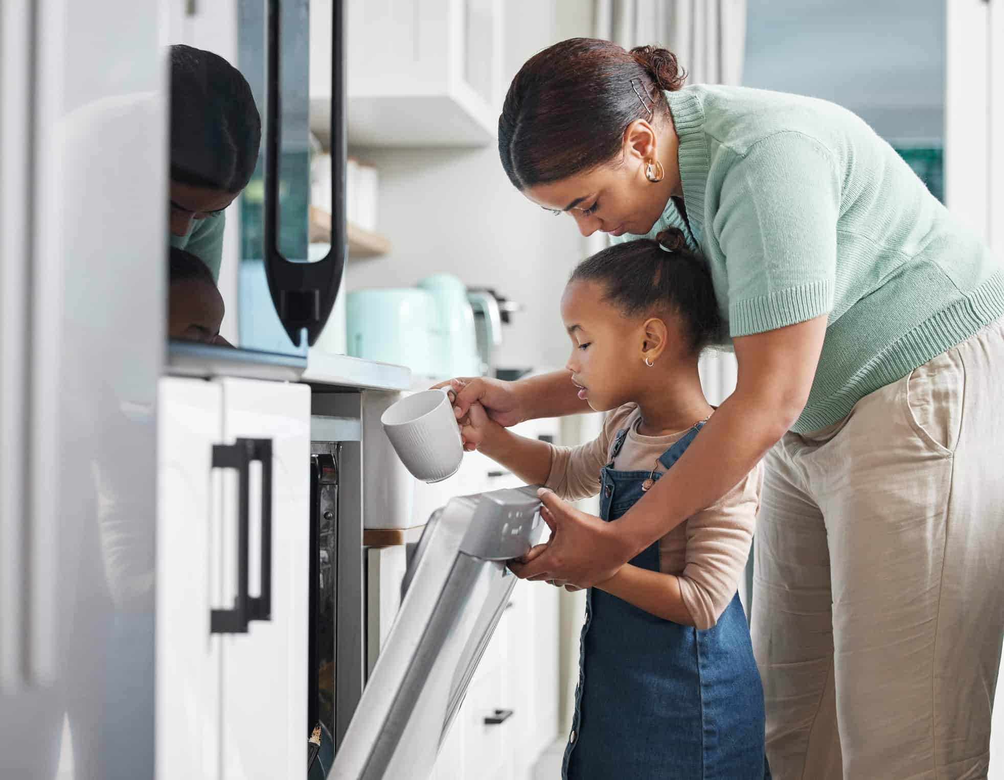 Shot of a little girl putting a cup into the dishwashing machine at home with her mother