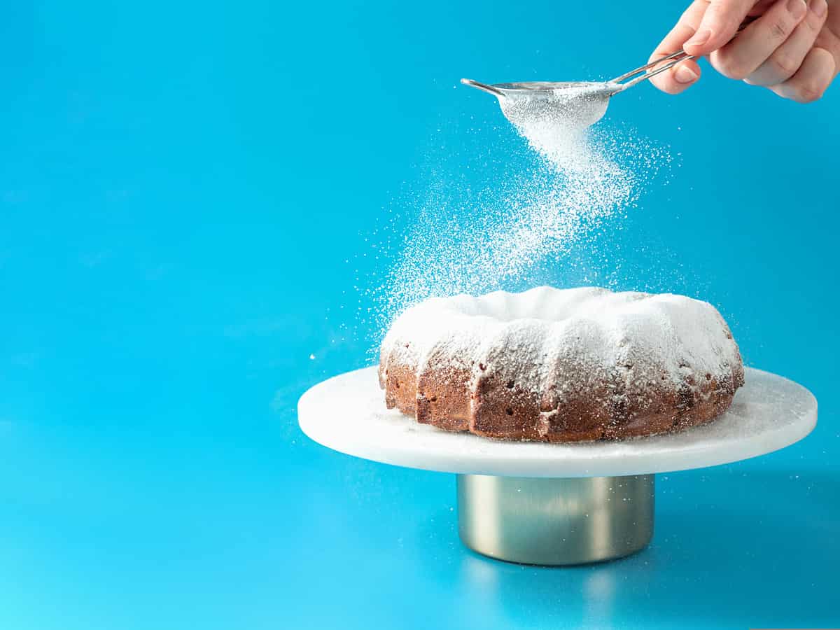 Female hand sprinkling sugar on bundt cake. Fructose vs glucose