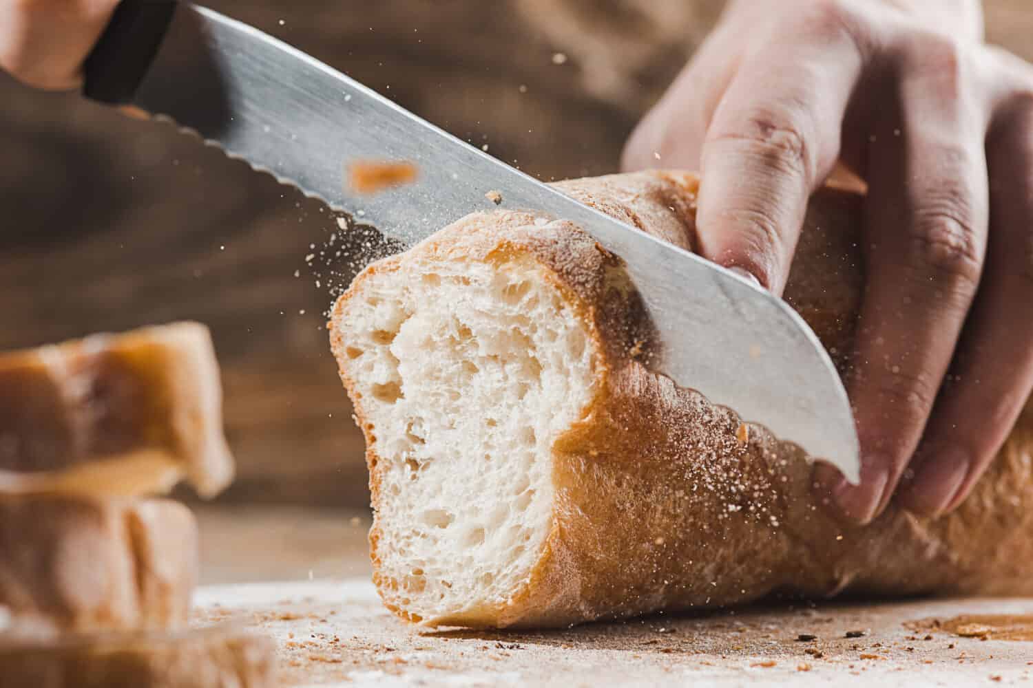 Whole grain bread put on kitchen wood plate with a chef holding gold knife for cut. Fresh bread on table close-up. Fresh bread on the kitchen table The healthy eating and traditional bakery concept
