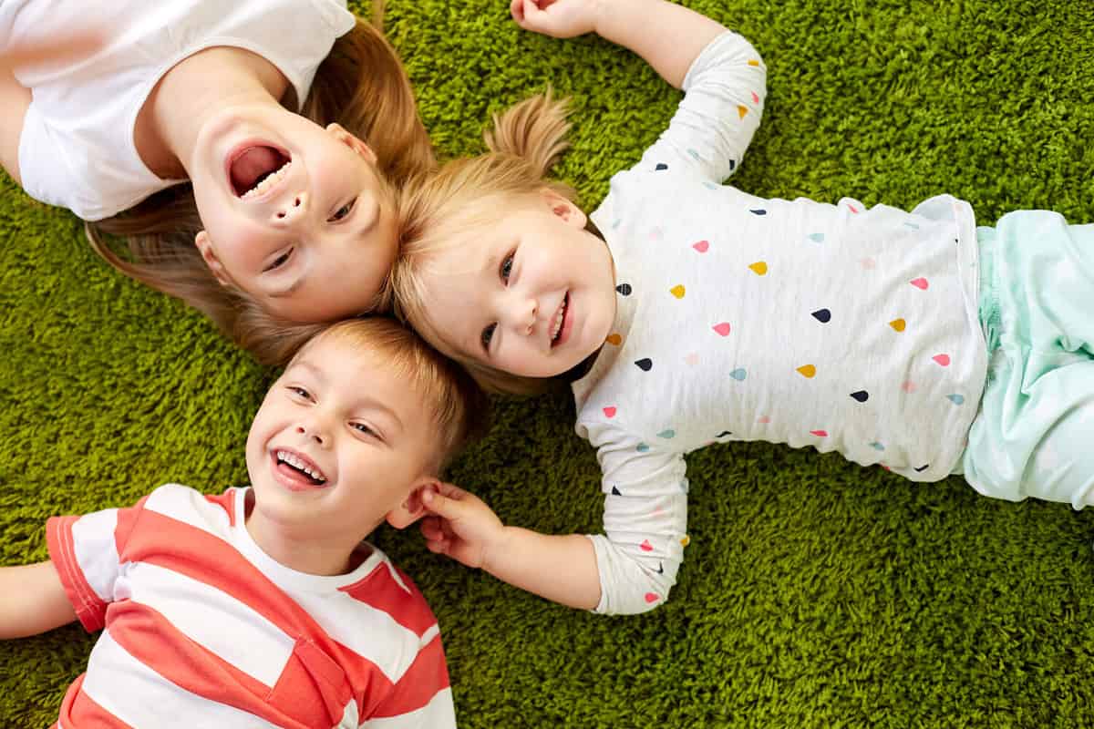 childhood, leisure and family concept - happy little kids lying on floor or carpet