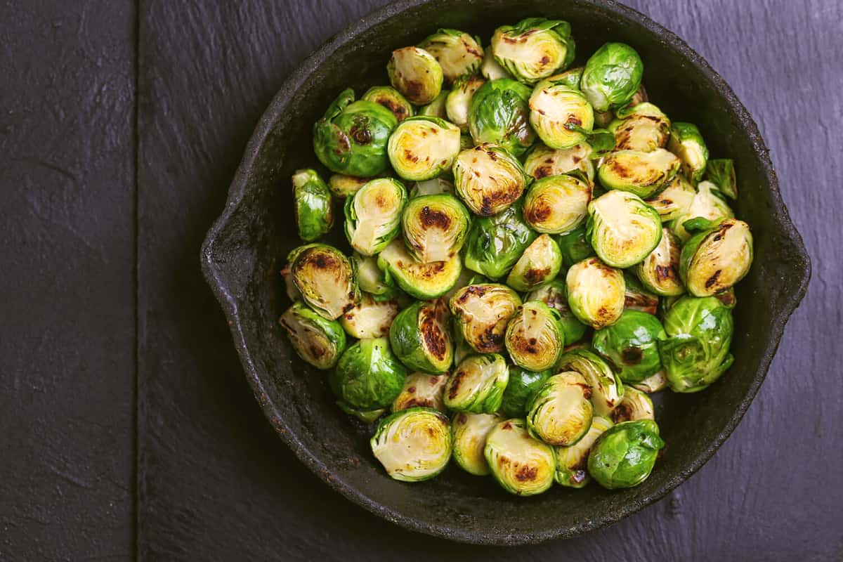 Vegetarian cuisine. Homemade Brussels Sprouts roasted with olive oil on black slate background. Copyspace, top view, flatlay.