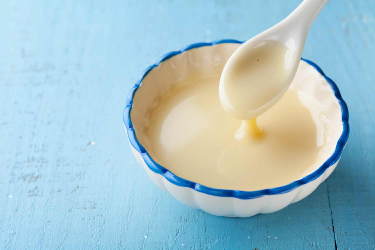 Bowl with pouring condensed milk or evaporated milk.