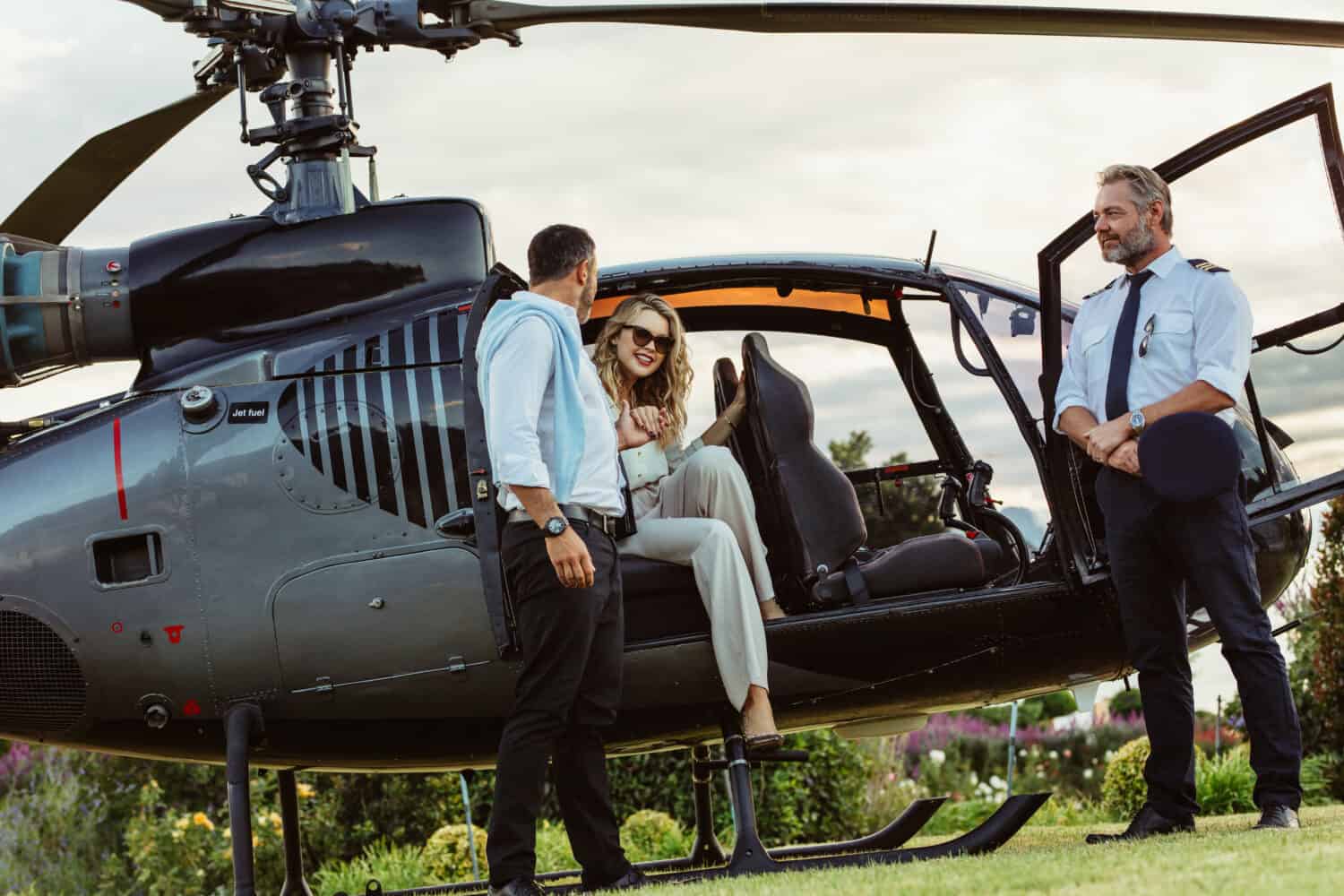 Beautiful woman getting down the helicopter with the help from her boyfriend. Couple disembarking their helicopter with pilot standing by.