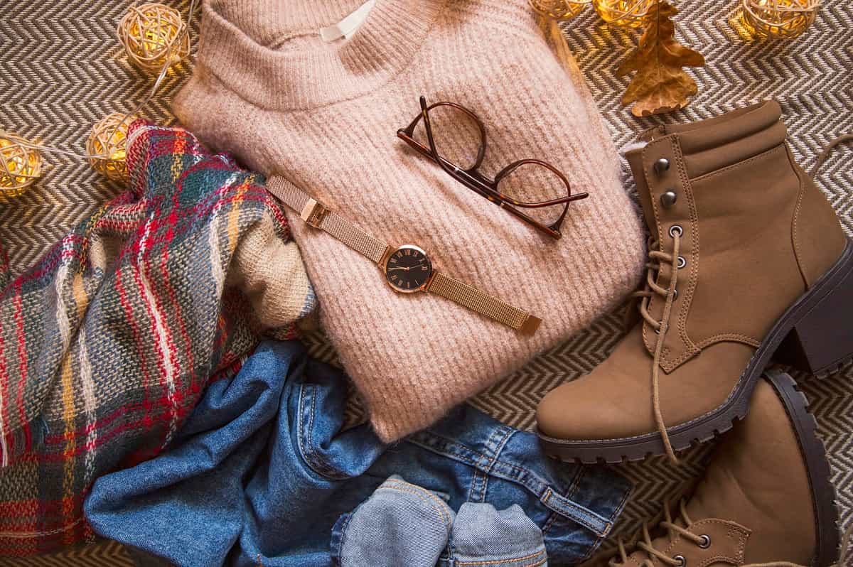 Autumn clothing outfit with sweater, jeans and boots, top view of fall/winter season outfit idea with glasses and watch accessory