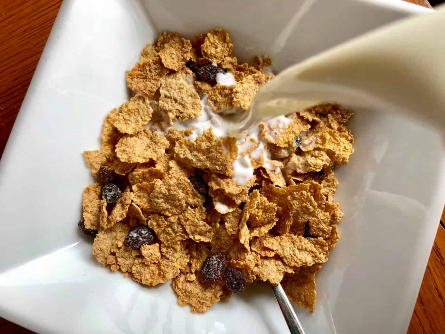 Milk being poured into a bowl of Raisin Bran