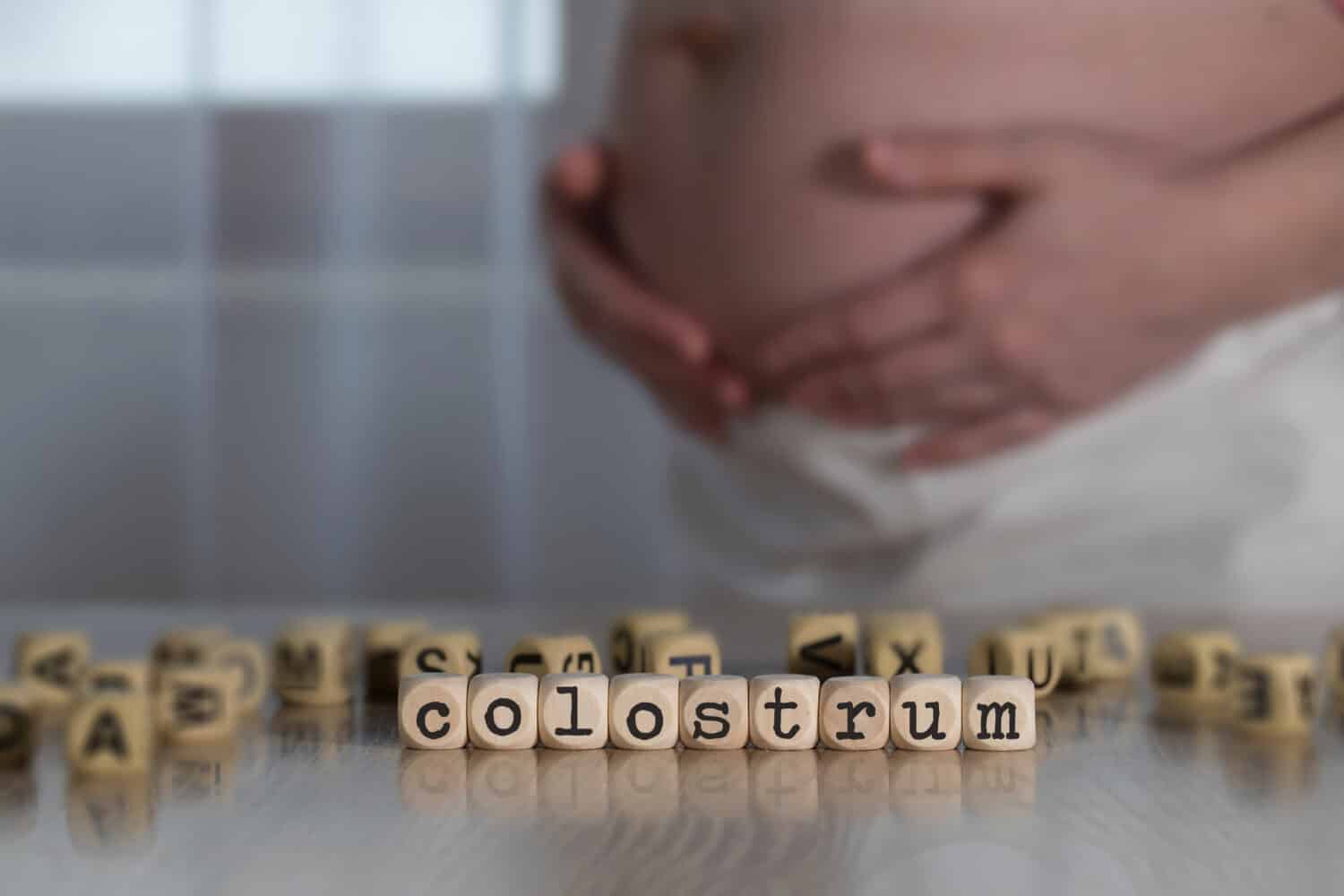 Word COLOSTRUM  composed of wooden letters. Pregnant woman in the background