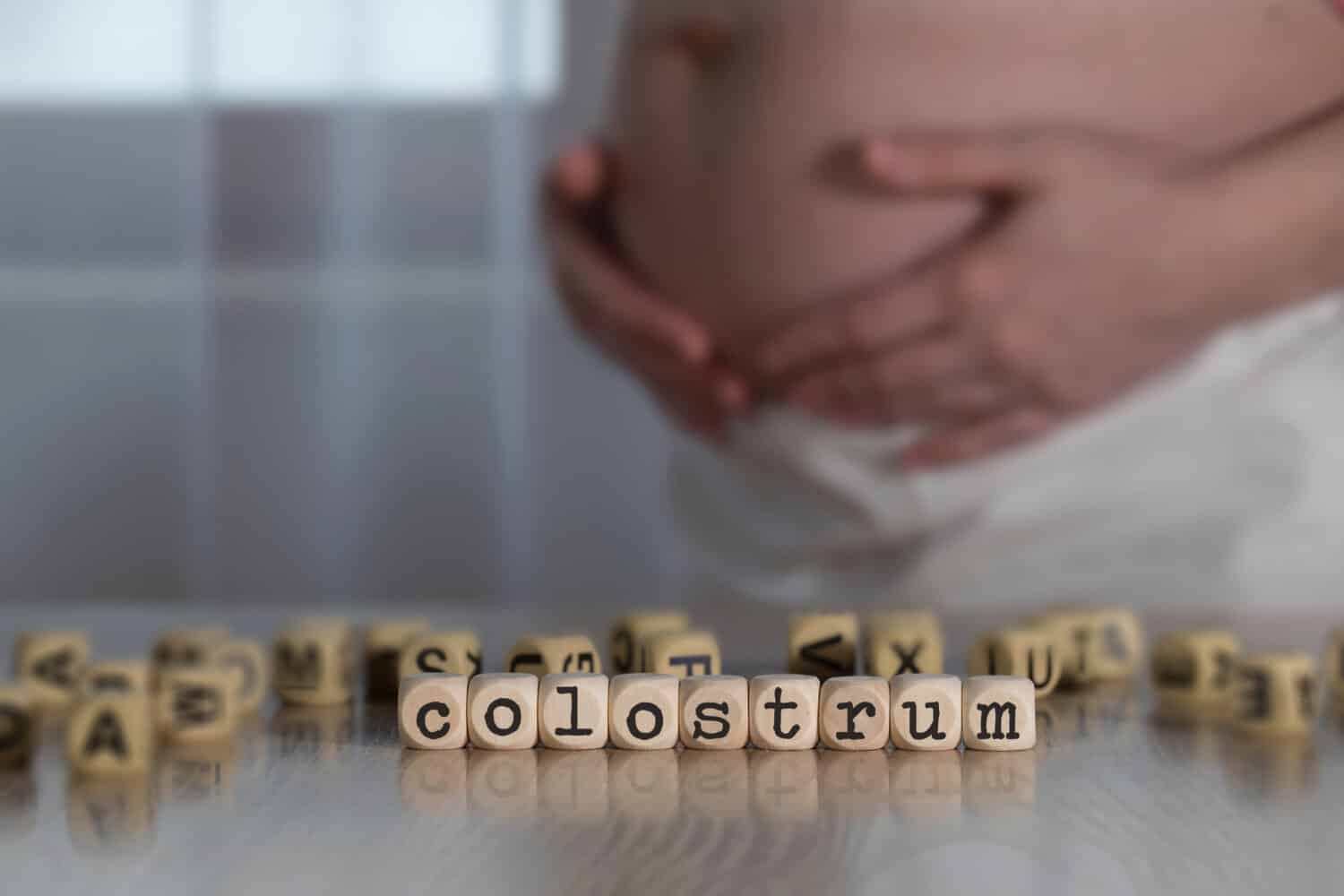 Word COLOSTRUM composed of wooden letters. Pregnant woman in the background