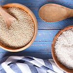 Rice and quinoa in wooden bowls on a blue wood table with tea towel and wooden spoon. Flat lay from directly above.