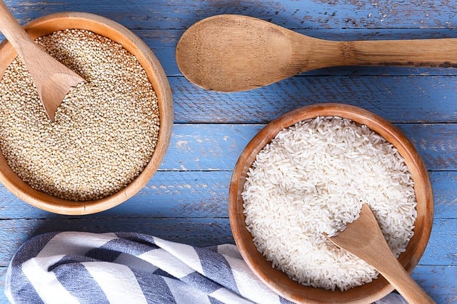 Rice and quinoa in wooden bowls on a blue wood table with tea towel and wooden spoon. Flat lay from directly above.