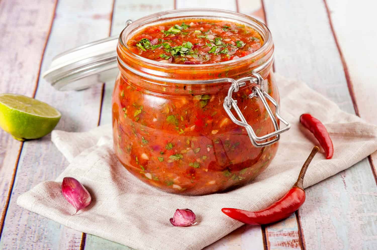 Tomato salsa in a glass jar. Homemade spicy tomato sauce with chilli, garlic and lime. Close up and horizontal orientation. 