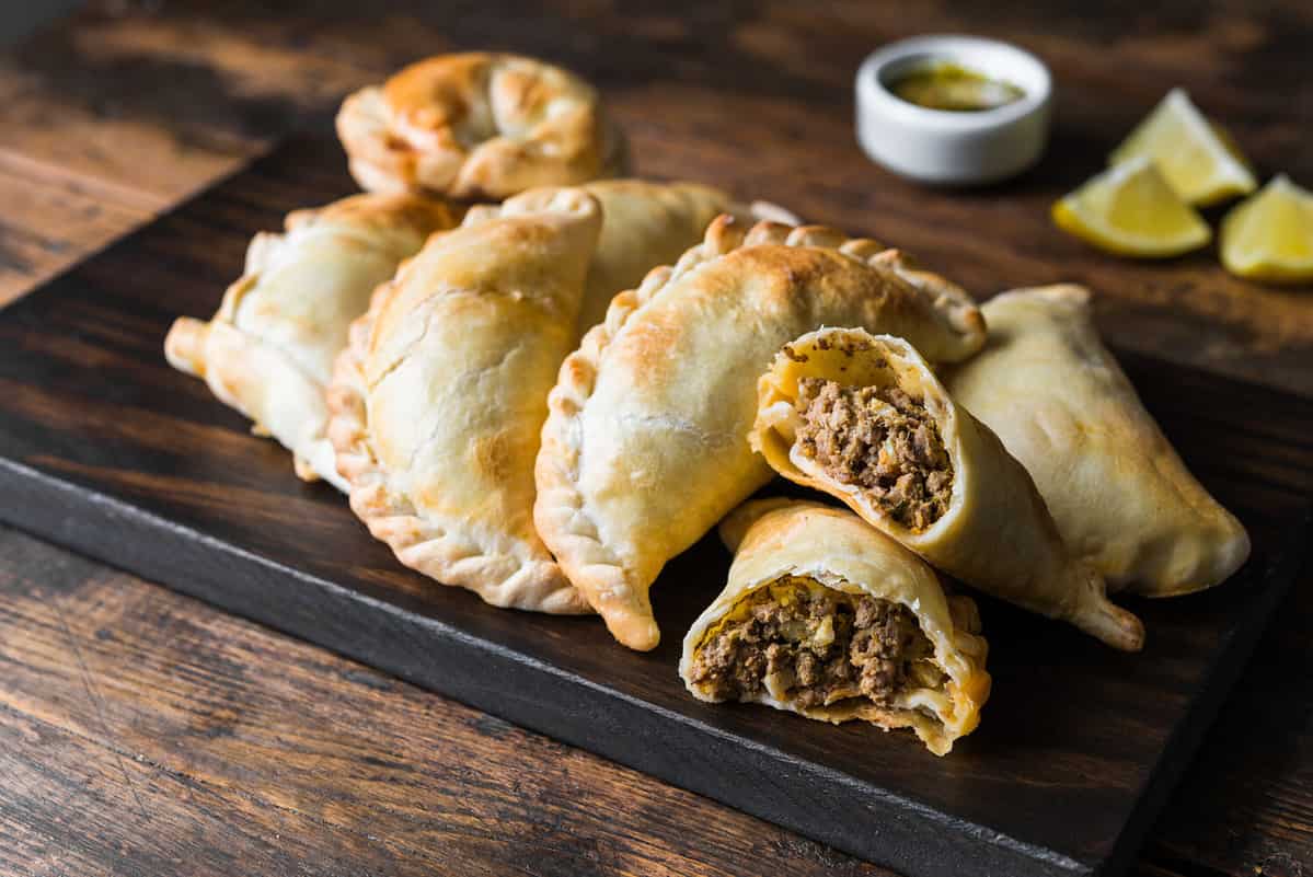 Traditional baked Argentine empanadas savoury pastries with meat beef stuffing against wooden background