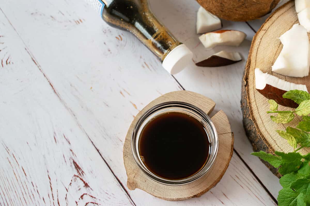 Coconut Aminos in a small glass bowl on a white wooden table. Soy sauce substitute. Light background