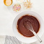 Flat lay. Step by step. Mixing ingredients together in a white mixing bowl to make unicorn chocolate cupcakes with buttercream frosting.