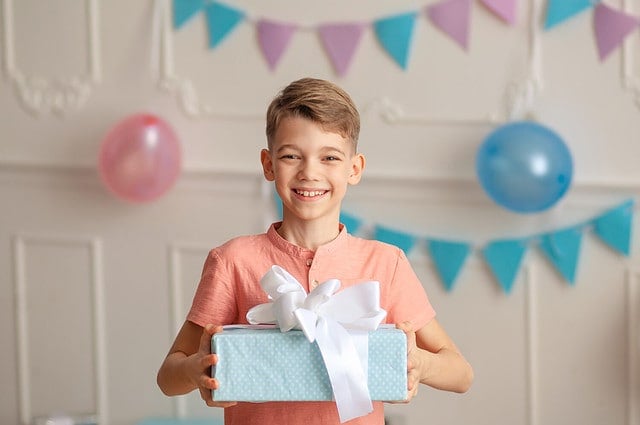 Happy Birthday Portrait of a happy cute boy of 8-9 years old in a festive decor with confetti and gifts.