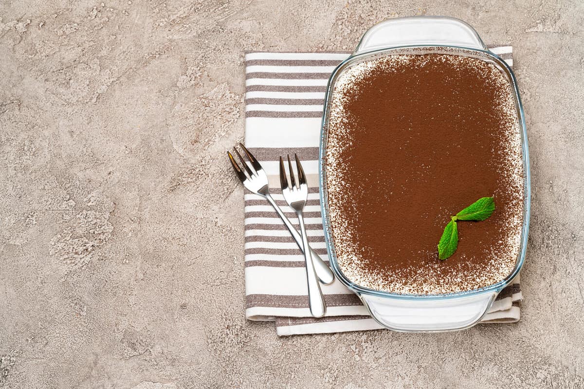 Traditional Italian Tiramisu dessert in glass baking dish on concrete background