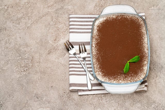 Traditional Italian Tiramisu dessert in glass baking dish on concrete background