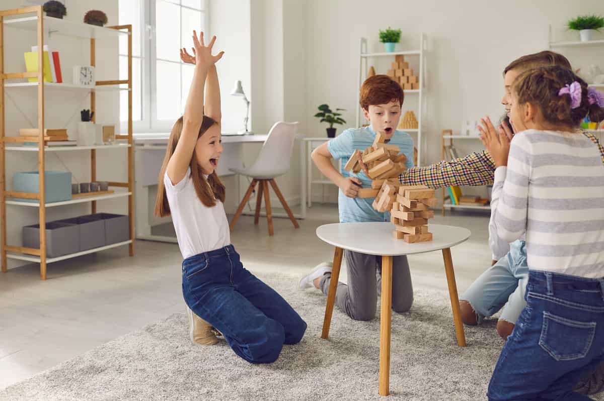 Oops, the tower is falling down! Group of happy excited 8-10 year old children playing wood block stacking board game at home or in an after school leisure club. Fun party activities for kids