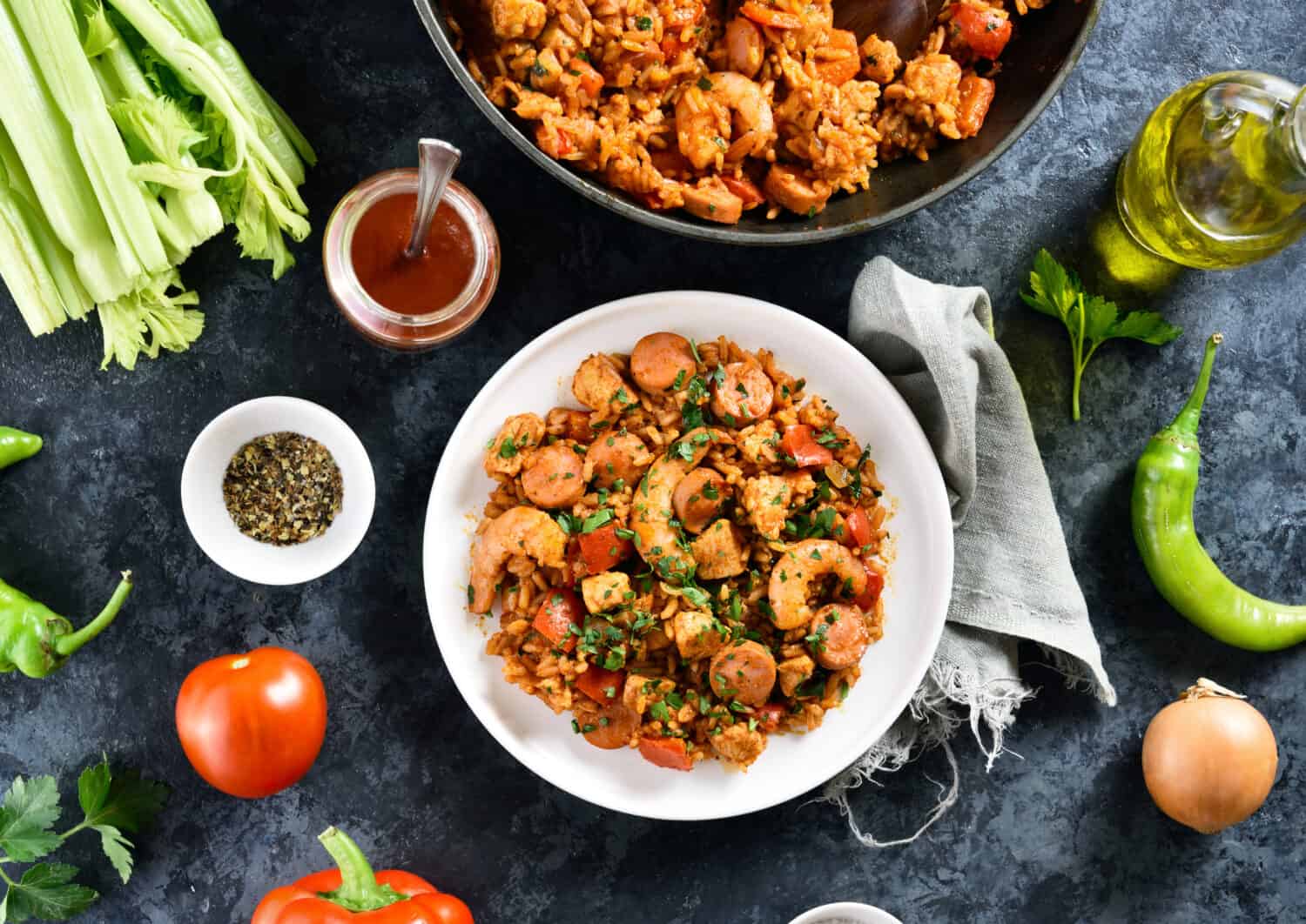 Creole jambalaya with rice, smoked sausages, chicken meat and vegetables on plate over blue stone background. Top view, flat lay, close up